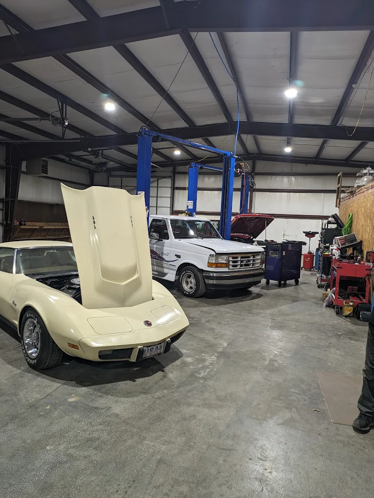 Classic Corvette Stingray with hood up beside a Ford F-250 in the shop
