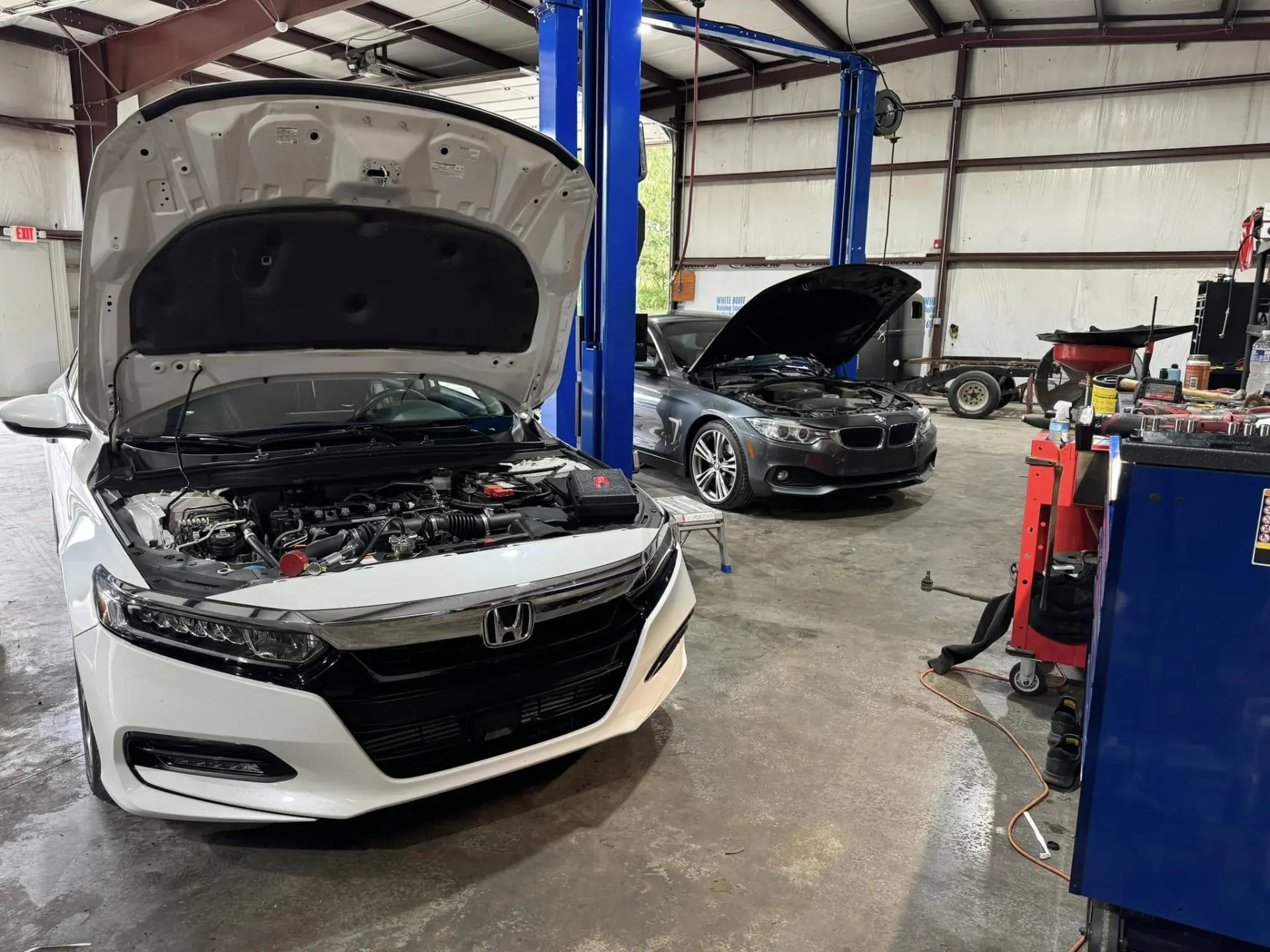 Honda Accord and BMW coupe with hoods up on the service floor